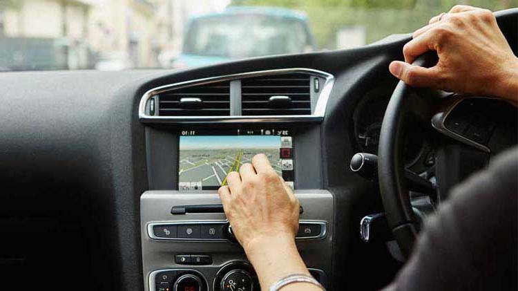 车里的人, 一只手放在方向盘上，另一只手与车载远程信息处理设备互动.
