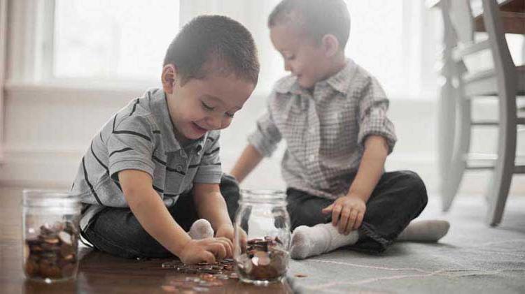 两个小男孩坐在地板上，把硬币放进罐子里，以保护他们的财产.