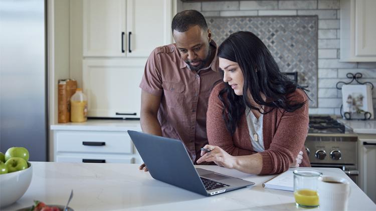A couple in their kitchen applying for car insurance on their laptop.