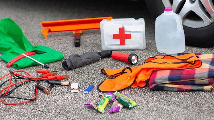 Jug of water, first aid kit, flashlight, 雨伞和其他应急用品被打包在街上的汽车轮胎旁边.